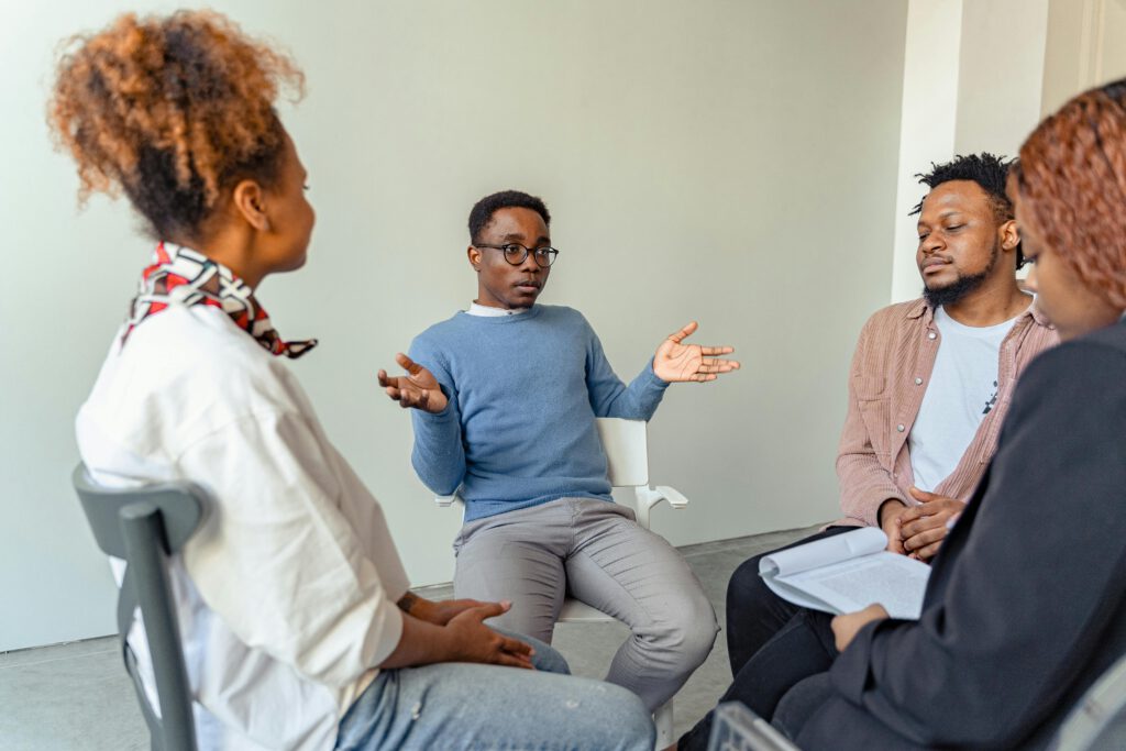 Diverse group therapy session with young adults and a mental health professional indoors.